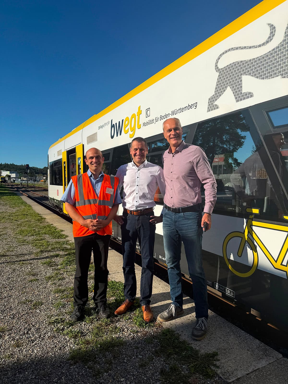 Christoph Stetter steht mit zwei Kollegen vor einem modernen Bus der BWEG in Baden-Württemberg, Deutschland, bei sonnigem Wetter.