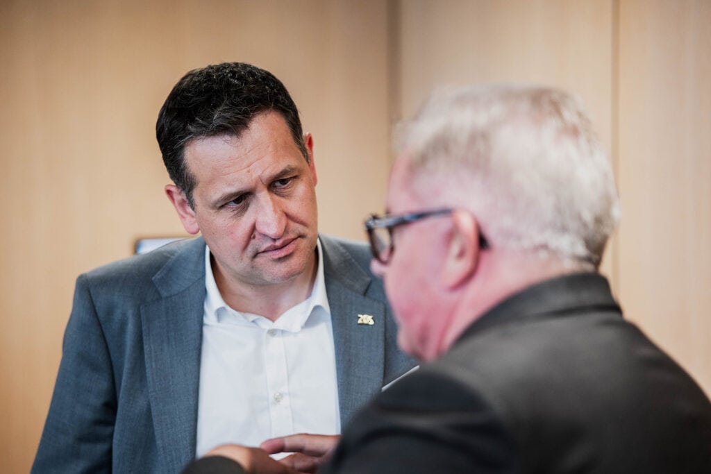 Christoph Stetter im Gespräch mit einem älteren Mann bei einem professionellen Meeting, zeigt Engagement und Fachkompetenz in einem geschäftlichen Umfeld.