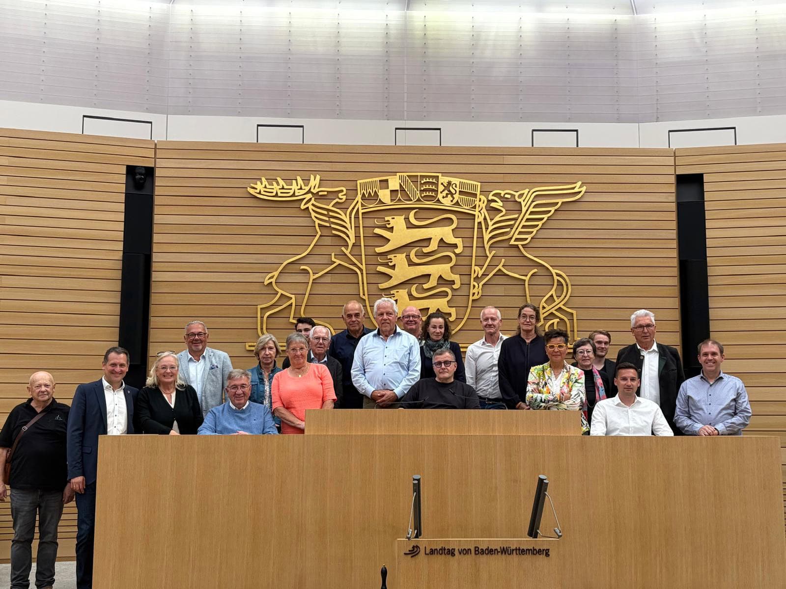 Gruppenfoto mit Christoph Stetter im Landtag Baden-Württemberg, im Hintergrund das Wappen des Bundeslandes.