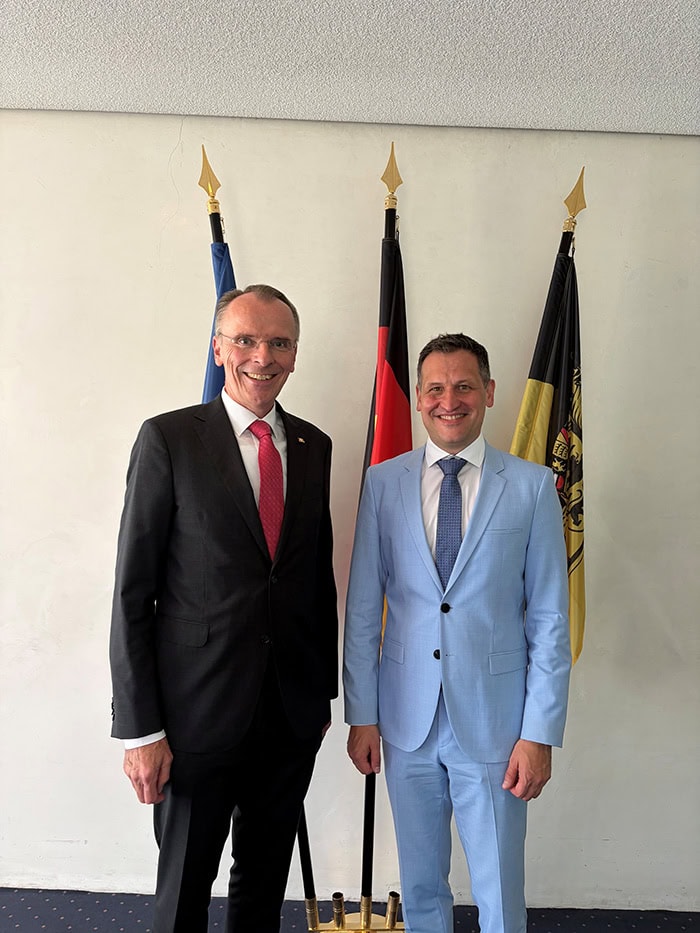Christoph Stetter und Prof. Dr. Alexander Bruns stehen vor deutschen und europäischen Flaggen bei einer offiziellen Veranstaltung.