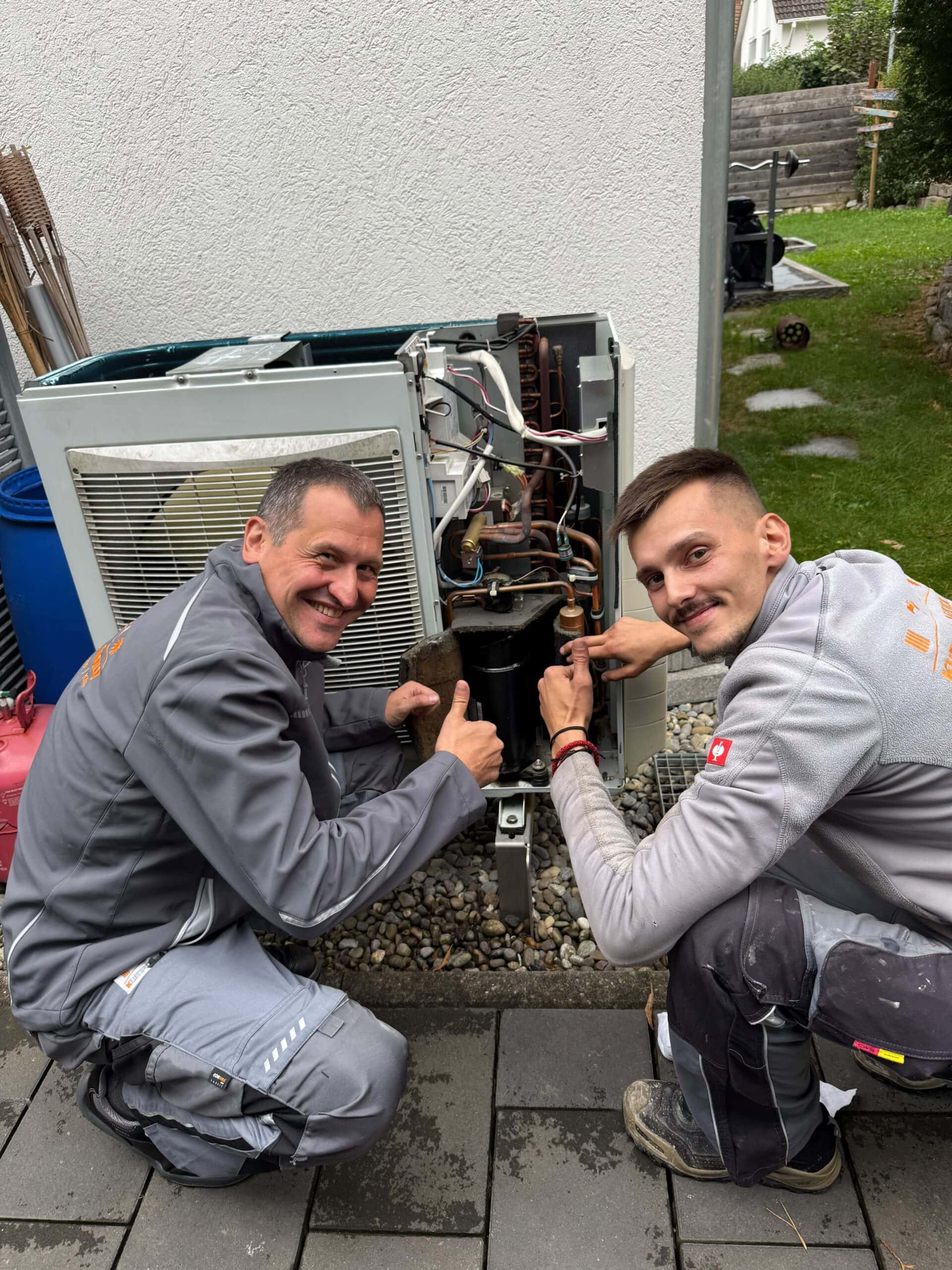 Zwei Handwerker reparieren eine Klimaanlage im Außenbereich eines Gebäudes, Fokus auf nachhaltige Lösungen im Handwerk.