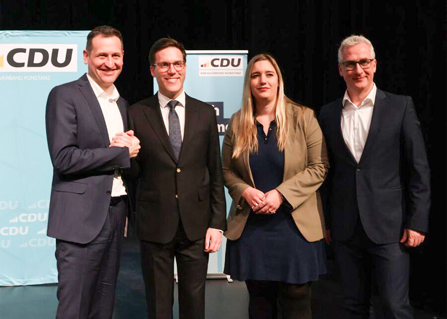 Vier Personen bei einer politischen Veranstaltung der CDU, alle in formeller Kleidung, stehen vor einem CDU-Logo, lächeln und posieren für die Kamera.