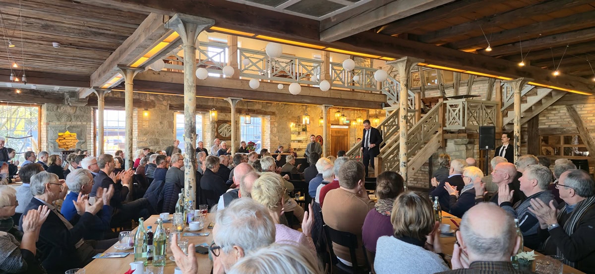 Eleganter Redner bei einer Veranstaltung im rustikalen Holzsaal, umgeben von einem begeisterten Publikum, typische Atmosphäre für Events mit Christoph Stetter in einem historischen Ambiente.
