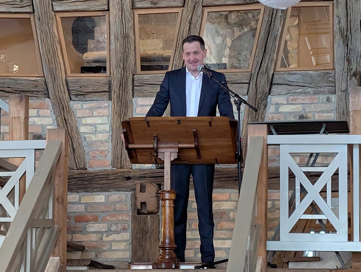 1. Moderner Vortragender bei einer Präsentation in einem rustikalen Ambiente, professionell gekleidet und sprechend vor Publikum.