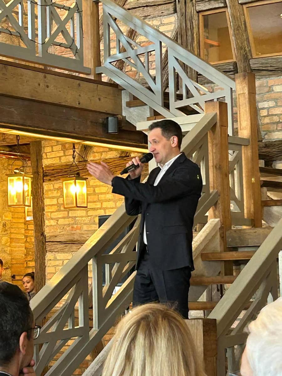 - Moderner Mann bei Rede mit Mikrofon in rustikalem Ambiente, Holztreppe, Steinwände, warmes Licht, Christoph Stetter, Dekor, Event, professionell, authentisch, Gastgeber, Präsentation, Veranstaltung, Speaker, Business, Lifestyle, Inneneinrichtung, Veranstaltungskonzept.