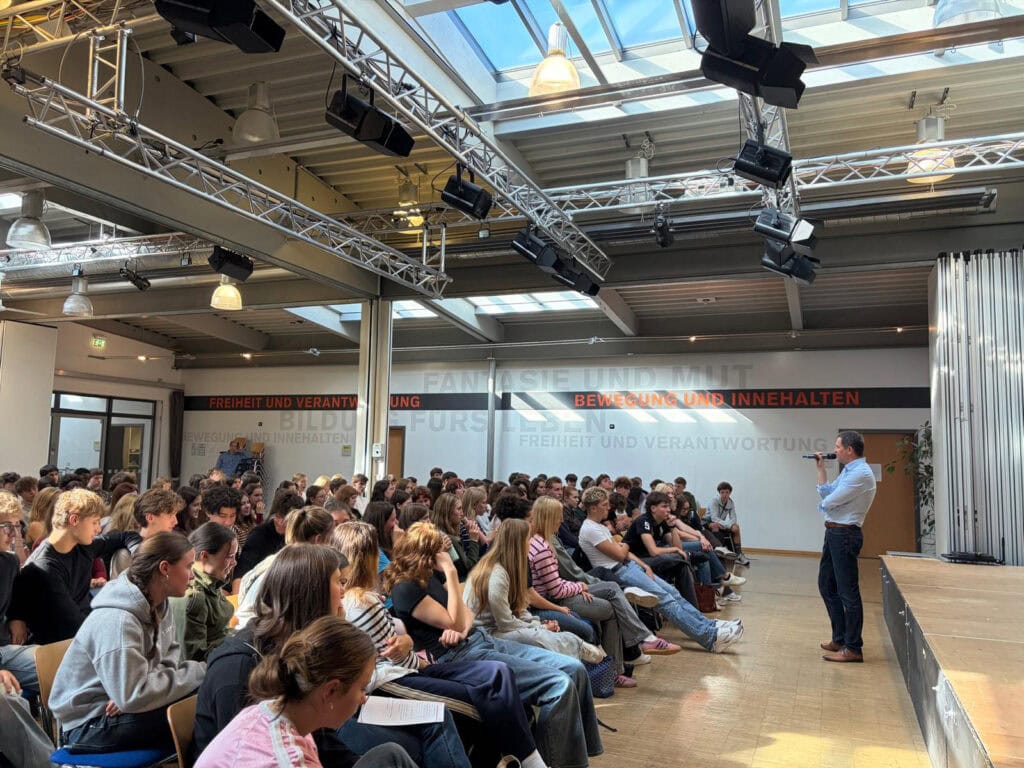 Christoph Stetter spricht vor einer Gruppe von Schülerinnen und Schülern in einem modernen Veranstaltungsraum.