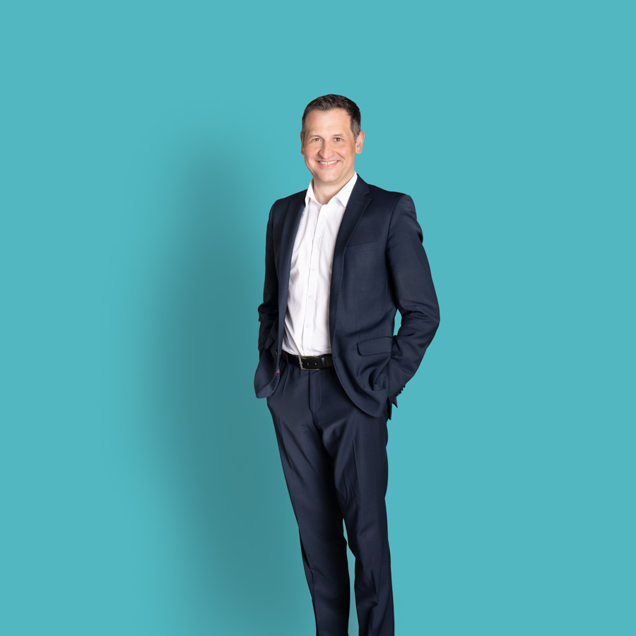 Foto des ganzen Körpers von Christoph Stetter, dem CDU-Kandidat zur Landtagswahl 2026, im blauen Anzug vor türkisfarbenem Hintergrund als Pressefoto