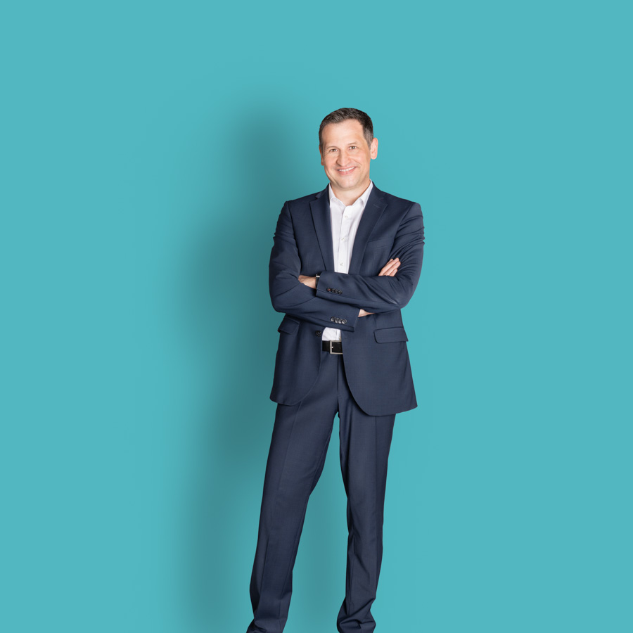 Foto des ganzen Körpers von Christoph Stetter, dem CDU-Kandidat zur Landtagswahl 2026, im blauen Anzug vor türkisfarbenem Hintergrund als Pressefoto