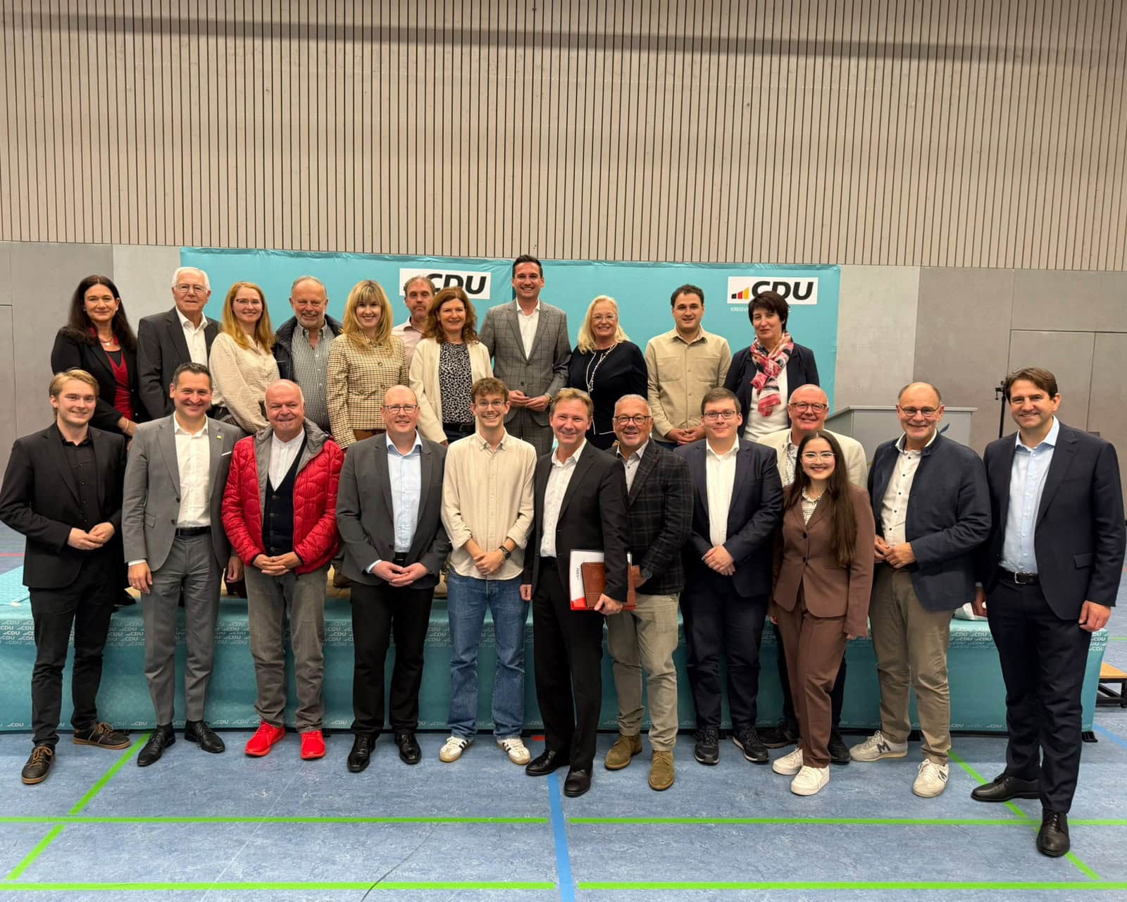 Gruppe von Fachleuten posiert gemeinsam für ein Gruppenbild bei einer Veranstaltung, im Hintergrund Banner mit Logo.